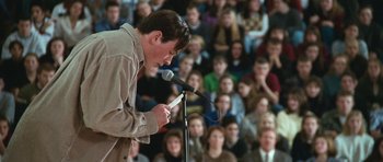 Movie still from “Election” (1999), directed by Alexander Payne – A man standing at a microphone with a crowd of people in the background; Medium shot, High angle