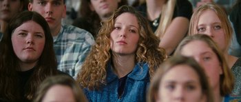 Movie still from “Election” (1999), directed by Alexander Payne – A woman with long curly hair sitting in a crowd of people; Close Up shot, Over the shoulder angle
