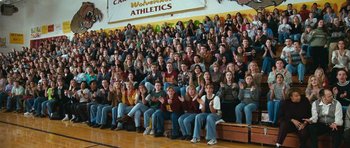 Movie still from “Election” (1999), directed by Alexander Payne – A group of people sitting in front of an audience at a gymnasium; Wide shot, High angle