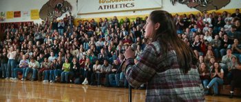 Movie still from “Election” (1999), directed by Alexander Payne – A woman is speaking in front of a crowd of people; Wide shot, High angle