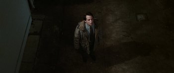 Movie still from “Election” (1999), directed by Alexander Payne – A man in a jacket and tie standing in a dark room; Wide shot, Overhead angle