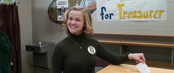 Movie still from “Election” (1999), directed by Alexander Payne – A woman sitting at a table smiling for the camera; Medium shot, High angle