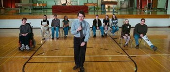 Movie still from “Election” (1999), directed by Alexander Payne – A group of people sitting in a circle and a man holding a microphone; Wide shot, High angle