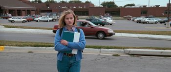 Movie still from “Election” (1999), directed by Alexander Payne – A girl is standing on the side of the road holding a book; Wide shot, Low angle