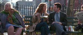 Two people are sitting on a bench and eating food