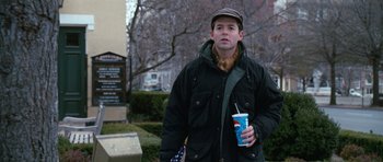 Movie still from “Election” (1999), directed by Alexander Payne – A man holding a cup of coffee while standing in a park; Medium shot, Over the shoulder angle