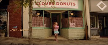 Movie still from “Dumplin'” (2018), directed by Anne Fletcher – A girl is standing in front of a donut shop; Wide shot, High angle