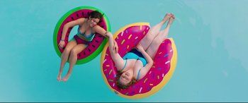 Movie still from “Dumplin'” (2018), directed by Anne Fletcher – Two women floating on a donut shaped pool float; Wide shot, Overhead angle