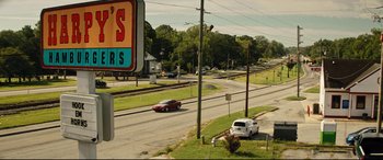 Movie still from “Dumplin'” (2018), directed by Anne Fletcher – Two cars driving down a street next to a street sign; Extreme Wide shot, High angle