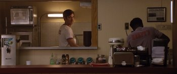 Movie still from “Dumplin'” (2018), directed by Anne Fletcher – A man standing in front of a mirror in a kitchen; Medium shot, Over the shoulder angle