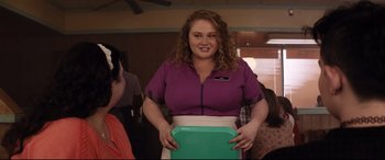 Movie still from “Dumplin'” (2018), directed by Anne Fletcher – A woman in a purple shirt holding a green tray; Medium shot, Over the shoulder angle