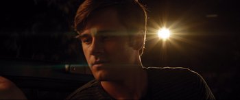 Movie still from “Dumplin'” (2018), directed by Anne Fletcher – A young man is looking at the camera with a glare of light in the background; Close Up shot, Low angle