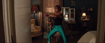 Movie still from “Dumplin'” (2018), directed by Anne Fletcher – A woman is playing a video game in a living room; Medium shot, Over the shoulder angle