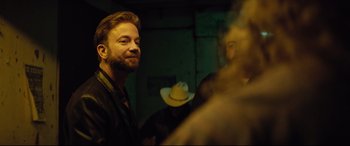 Movie still from “Dumplin'” (2018), directed by Anne Fletcher – A man with a beard and a cowboy hat in a room; Close Up shot, Over the shoulder angle