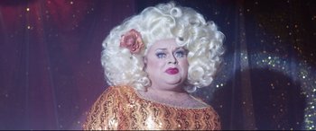 Movie still from “Dumplin'” (2018), directed by Anne Fletcher – A drag queen with a big white wig and a flower in her hair; Close Up shot, Low angle