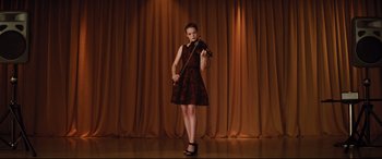 Movie still from “Dumplin'” (2018), directed by Anne Fletcher – A woman in a red dress holding a violin on a stage; Wide shot, Low angle