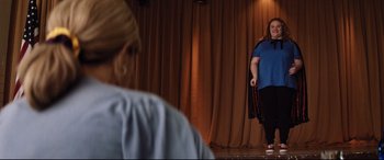 Movie still from “Dumplin'” (2018), directed by Anne Fletcher – A woman standing in front of another woman on a stage; Wide shot, Over the shoulder angle