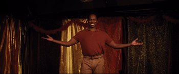 Movie still from “Dumplin'” (2018), directed by Anne Fletcher – A man standing in front of a gold curtain; Medium shot, Low angle