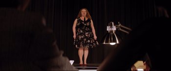 Movie still from “Dumplin'” (2018), directed by Anne Fletcher – A woman standing on a stage wearing a black dress; Wide shot, Over the shoulder angle