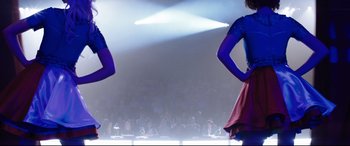 Movie still from “Dumplin'” (2018), directed by Anne Fletcher – Two women are standing in front of an audience; Medium shot, Low angle