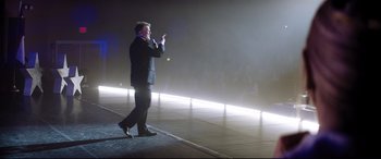 Movie still from “Dumplin'” (2018), directed by Anne Fletcher – A man standing on a stage in front of an audience; Wide shot, Low angle