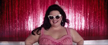 Movie still from “Dumplin'” (2018), directed by Anne Fletcher – A woman wearing a pink and white checkered dress and sunglasses; Medium shot, Low angle