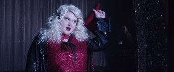 Movie still from “Dumplin'” (2018), directed by Anne Fletcher – A woman with blonde hair wearing a red jacket; Medium shot, Over the shoulder angle