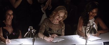 Movie still from “Dumplin'” (2018), directed by Anne Fletcher – A woman writing on a piece of paper at a table; Medium shot, Over the shoulder angle