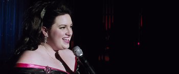 Movie still from “Dumplin'” (2018), directed by Anne Fletcher – A woman is holding a microphone and smiling; Close Up shot, Over the shoulder angle