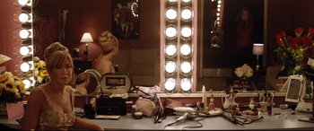 Movie still from “Dumplin'” (2018), directed by Anne Fletcher – A woman sitting in front of a lighted mirror in a room; Wide shot, High angle