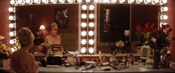 Movie still from “Dumplin'” (2018), directed by Anne Fletcher – A woman sitting in front of a makeup mirror in a room; Medium shot, High angle