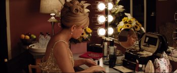 Movie still from “Dumplin'” (2018), directed by Anne Fletcher – A woman sitting in front of a mirror with make - up on; Medium shot, High angle
