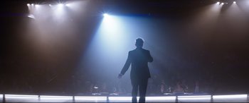 Movie still from “Dumplin'” (2018), directed by Anne Fletcher – A man standing in front of an audience on a stage; Wide shot, Low angle