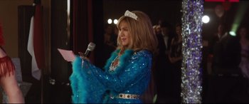Movie still from “Dumplin'” (2018), directed by Anne Fletcher – A woman in a blue dress holding a microphone; Medium shot, Over the shoulder angle