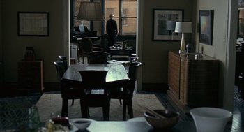 Movie still from “Elegy” (2008), directed by Isabel Coixet – A person standing in a room with a table and chairs in front of a window; Wide shot, Over the shoulder angle