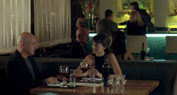 Movie still from “Elegy” (2008), directed by Isabel Coixet – A woman sitting at a table in front of a glass of red wine; Medium shot, Over the shoulder angle