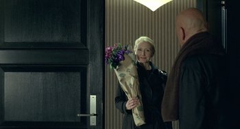 Movie still from “Elegy” (2008), directed by Isabel Coixet – A woman holding a bouquet of flowers in front of a door; Medium shot, Over the shoulder angle