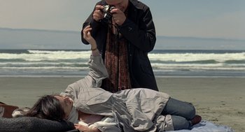 Movie still from “Elegy” (2008), directed by Isabel Coixet – A man taking a picture of a woman laying on the beach; Medium shot, Low angle