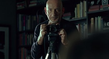 Movie still from “Elegy” (2008), directed by Isabel Coixet – A man holding a camera in front of a book shelf; Close Up shot, Low angle