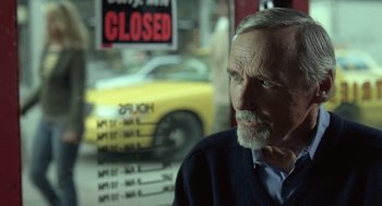 Movie still from “Elegy” (2008), directed by Isabel Coixet – An older man sitting in front of a closed store window; Close Up shot, Over the shoulder angle