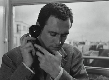 Movie still from “Elevator to the Gallows” (1958), directed by Louis Malle – A black and white photo of a man adjusting his ear piece; Close Up shot, High angle
