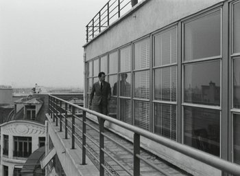 Movie still from “Elevator to the Gallows” (1958), directed by Louis Malle – A man standing on a railing next to a building; Wide shot, Low angle