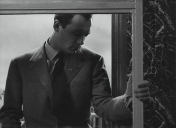 Movie still from “Elevator to the Gallows” (1958), directed by Louis Malle – A black and white photo of a man in a suit looking out of a window; Medium shot, Low angle