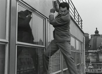 Movie still from “Elevator to the Gallows” (1958), directed by Louis Malle – A black and white photo of a man hanging on to a window; Medium shot, Low angle