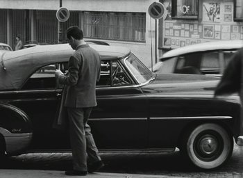 Movie still from “Elevator to the Gallows” (1958), directed by Louis Malle – A black and white photo of a man standing next to a car; Wide shot, Low angle