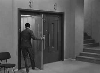 Movie still from “Elevator to the Gallows” (1958), directed by Louis Malle – A black and white photo of a man opening a door to an elevator; Wide shot, High angle