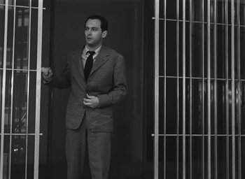 Movie still from “Elevator to the Gallows” (1958), directed by Louis Malle – A black and white photo of a man standing in front of bars; Medium shot, Low angle