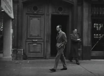 Movie still from “Elevator to the Gallows” (1958), directed by Louis Malle – A man walking down the street in front of a building; Wide shot, Low angle