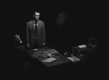Movie still from “Elevator to the Gallows” (1958), directed by Louis Malle – A man standing in front of a group of people; Wide shot, Over the shoulder angle