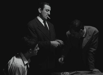 Movie still from “Elevator to the Gallows” (1958), directed by Louis Malle – A man in a black suit smoking a cigarette; Medium shot, Over the shoulder angle